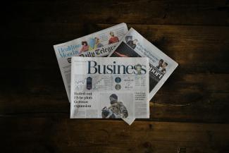 a stack of newspapers sitting on top of a wooden table by Annie Spratt courtesy of Unsplash.