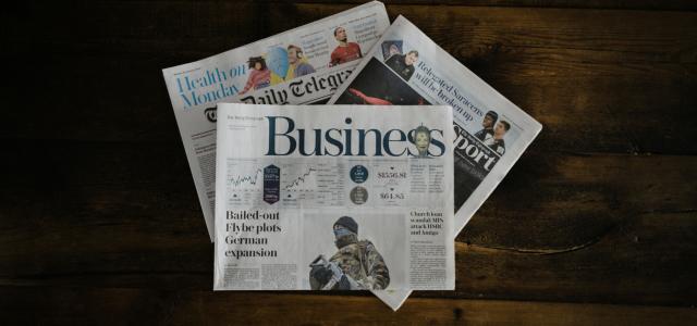 a stack of newspapers sitting on top of a wooden table by Annie Spratt courtesy of Unsplash.